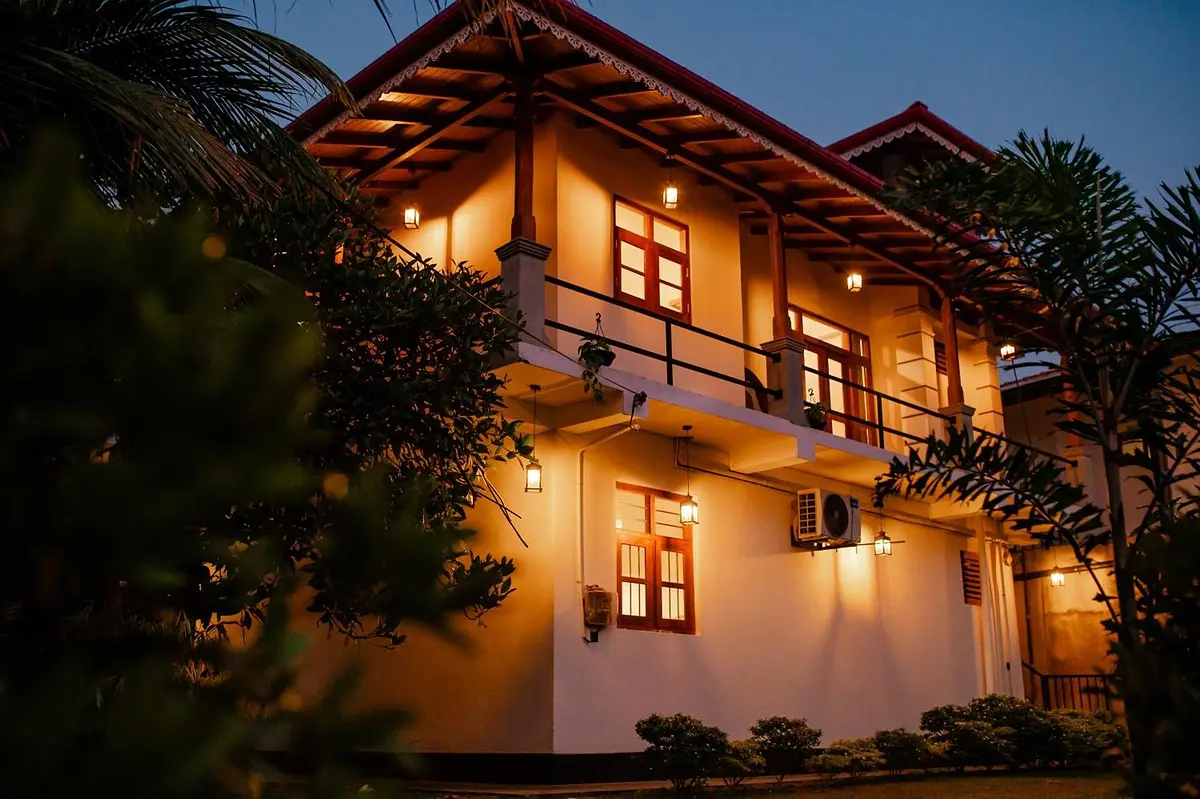 Villa 4Eyes at dusk, the two-storey white villa glowing with warm lights beneath the palms