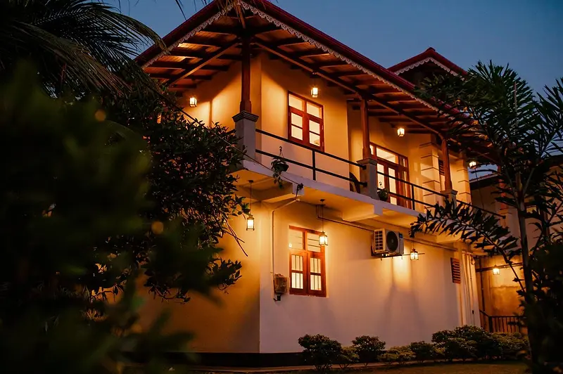 Villa 4Eyes at dusk, the two-storey white villa glowing with warm lights beneath the palms
