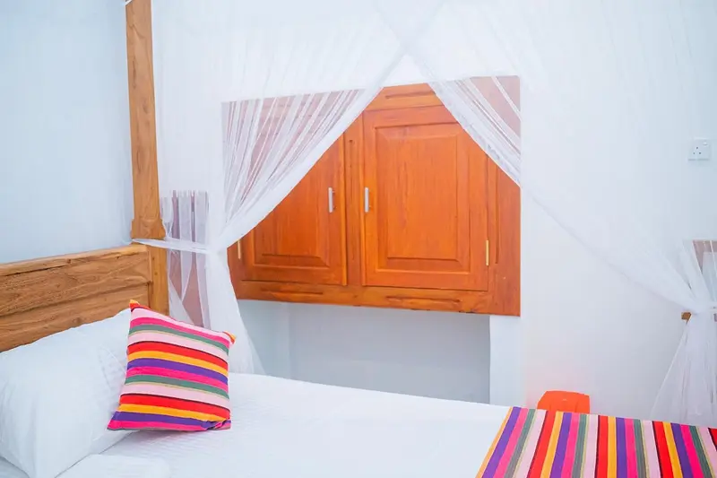 White linen and a bright striped cushion beneath the mosquito net
