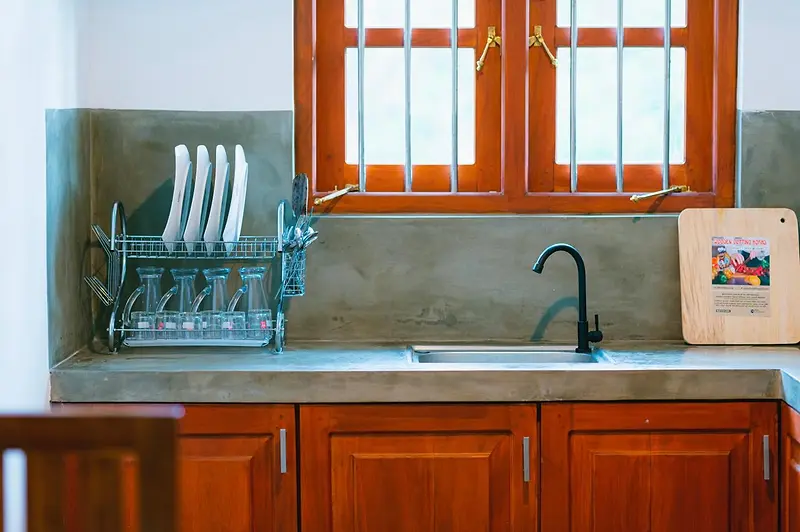 Kitchen sink and dish rack beneath teak-framed windows